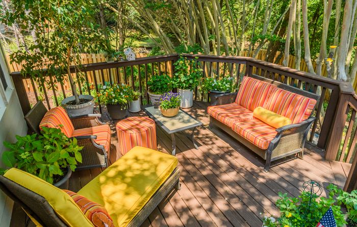 A wooded back porch with iron and wicker furniture, covered in bright orange and yellow striped cushions.
